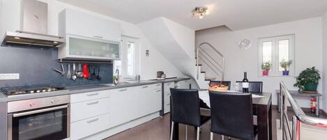 Et moderne køkken med hvide skabe, en gasovn og et spiseområde med to sorte stole.