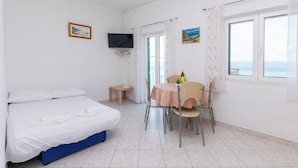 A hotel room with a bed, a small table with a bottle, a chair, a TV mounted on the wall, and a window with a view. - Apartments Marko (Omis)
