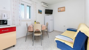 A compact room with a kitchenette, a dining table with chairs, a bed with a blue and yellow blanket, a TV, and two framed pictures on the wall. - Apartments Marko (Omis)