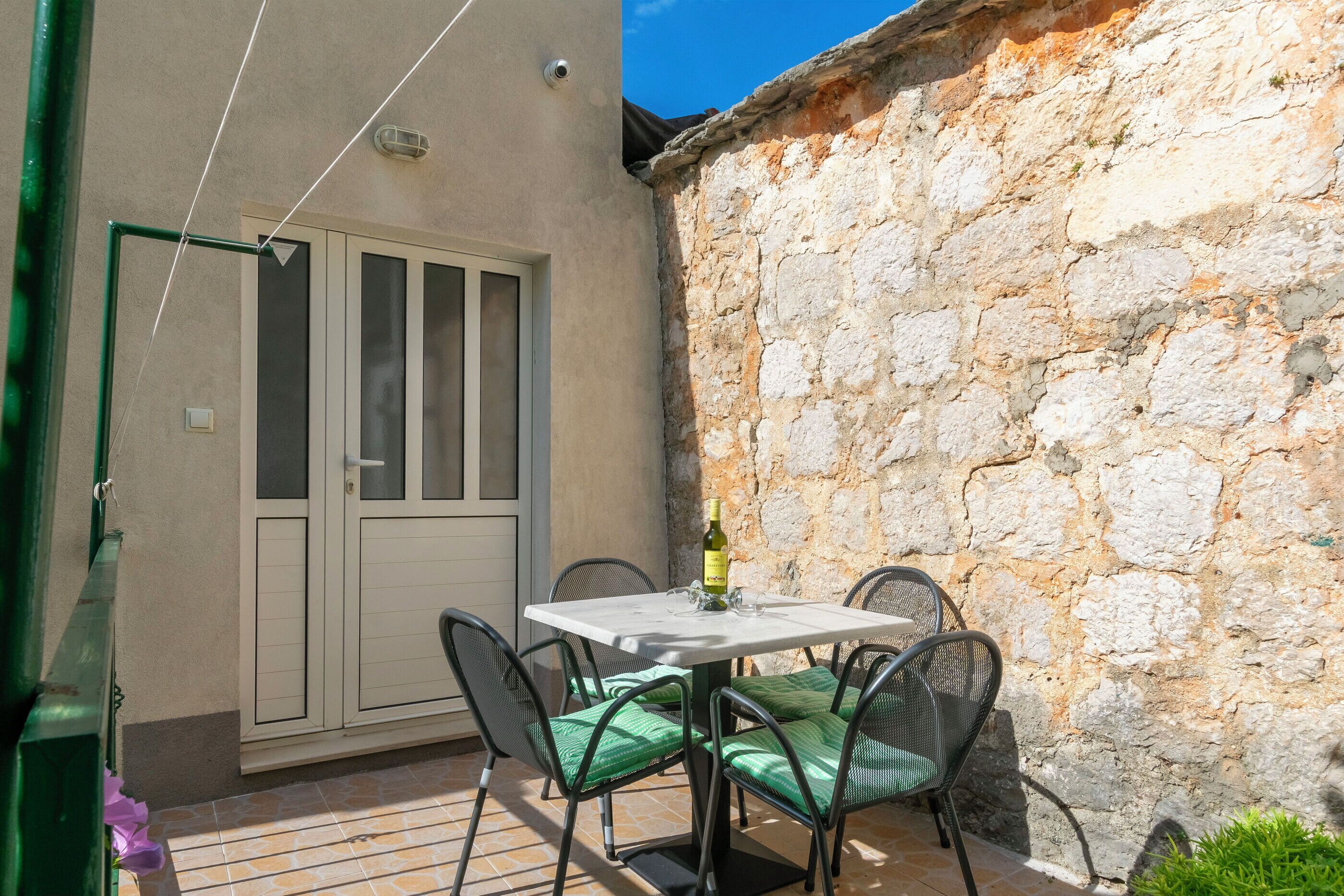 Une terrasse avec une table et des chaises, une bouteille de vin et un mur en pierre.