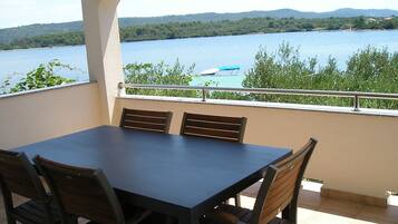 Balcón con mesa y sillas con vistas a un lago con botes y vegetación.