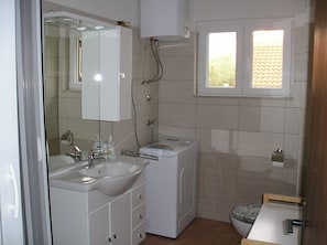 A compact bathroom with a sink, mirror, toilet, and a window.