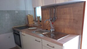 A compact kitchen with a stove, sink, and wooden countertop. - Apartments Tonci (Kali)
