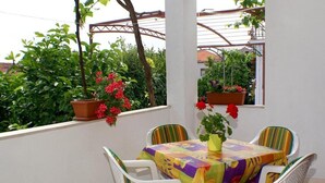 A covered patio with a table and chairs, surrounded by potted plants and a view of greenery. - Apartments Stuk (Orebic)