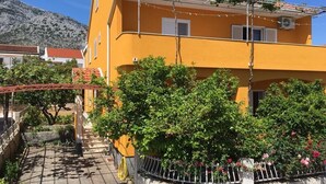 A yellow building with a red-tiled roof, surrounded by greenery and a paved area. - Apartments Stuk (Orebic)