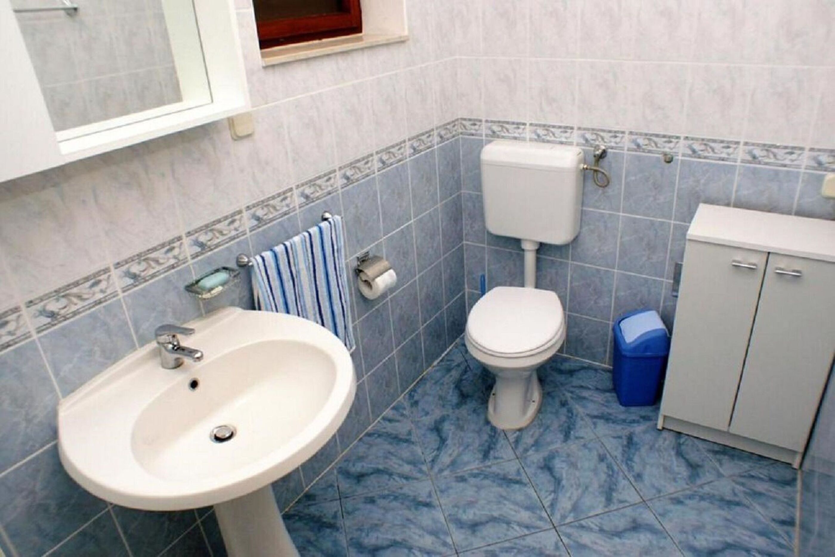 A bathroom with a sink, toilet, and cabinet.