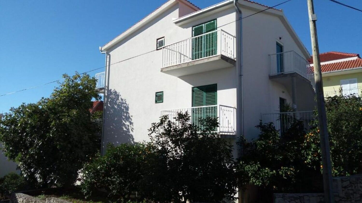 A two-story building with a balcony, surrounded by greenery.