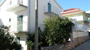 Un edificio residencial con balcones, un muro de piedra y un árbol de hojas verdes.