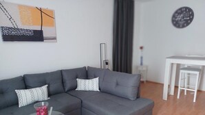 A modern living room with a grey sectional sofa, a glass coffee table, and a white dining area with a small table and two chairs. - Apartment Marijica (Okrug)