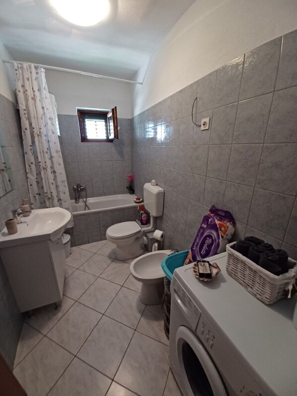 A compact bathroom with a sink, toilet, bathtub, and a washing machine. - Apartment Marijica (Okrug)
