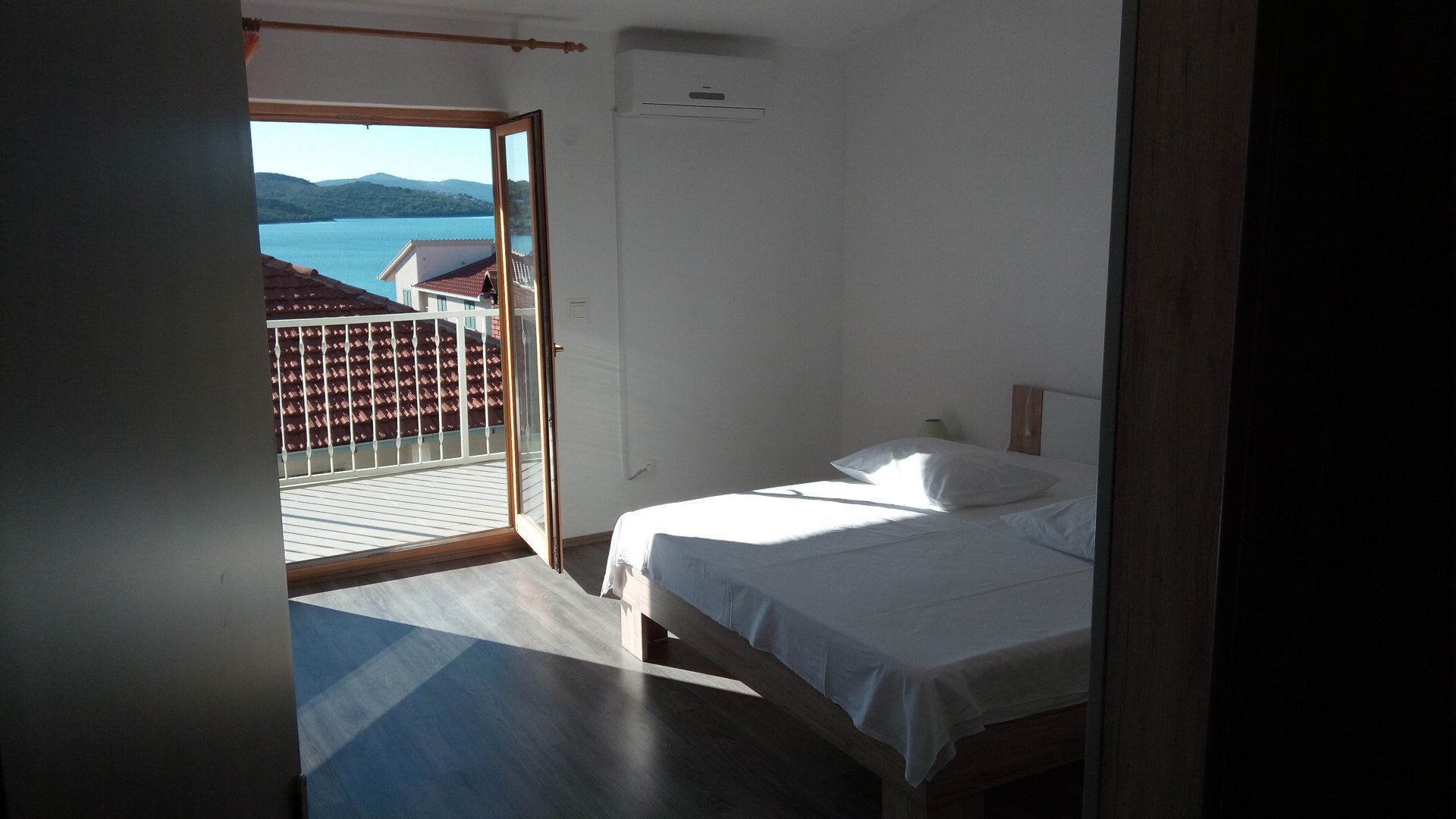 A bedroom with a bed, a view of a balcony, and a window.