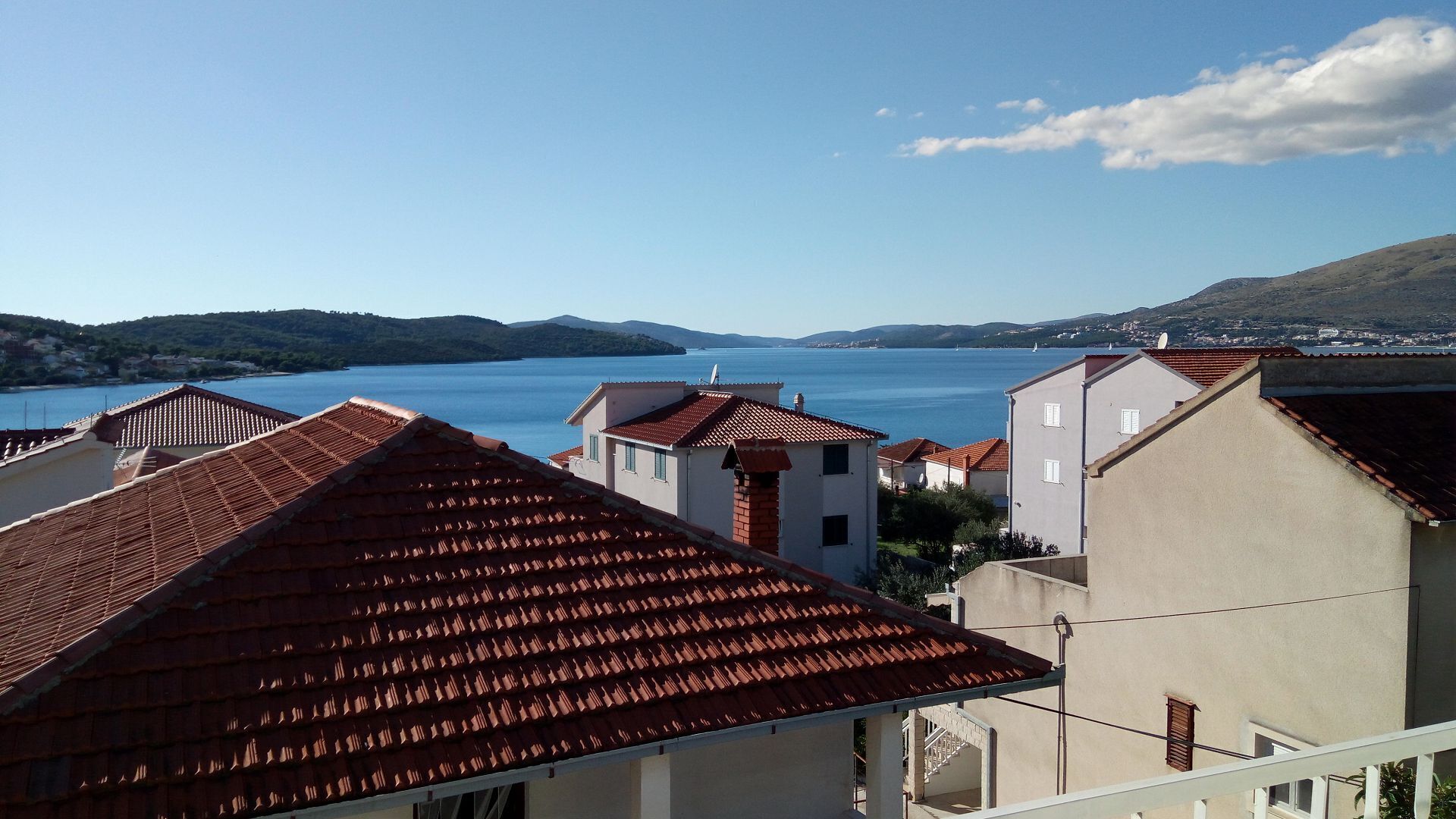 Una cittadina costiera con edifici a tetti in terracotta, un mare cristallino e dolci colline sullo sfondo.