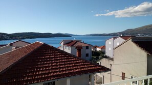Un pueblo costero con edificios de tejas rojas, un mar azul cristalino y colinas lejanas.