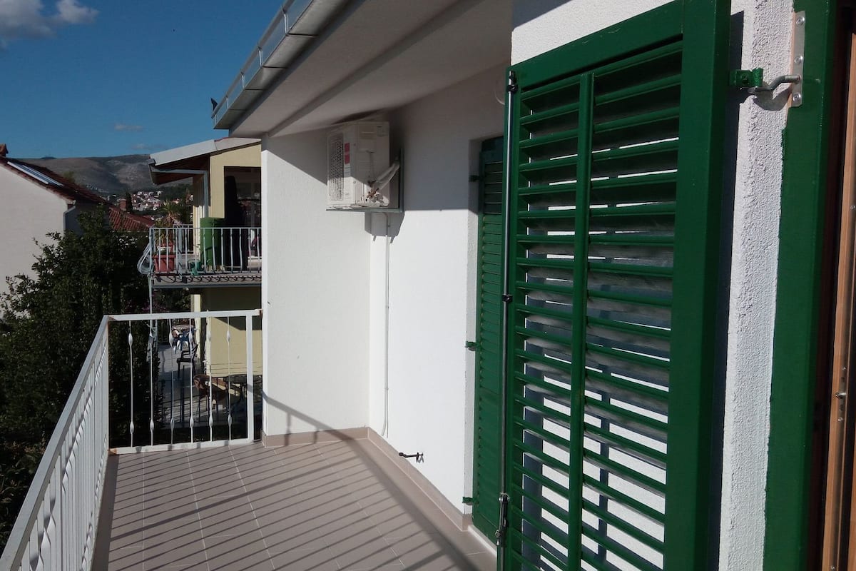 A balcony with a wooden floor, a white railing, and a green shutter door.