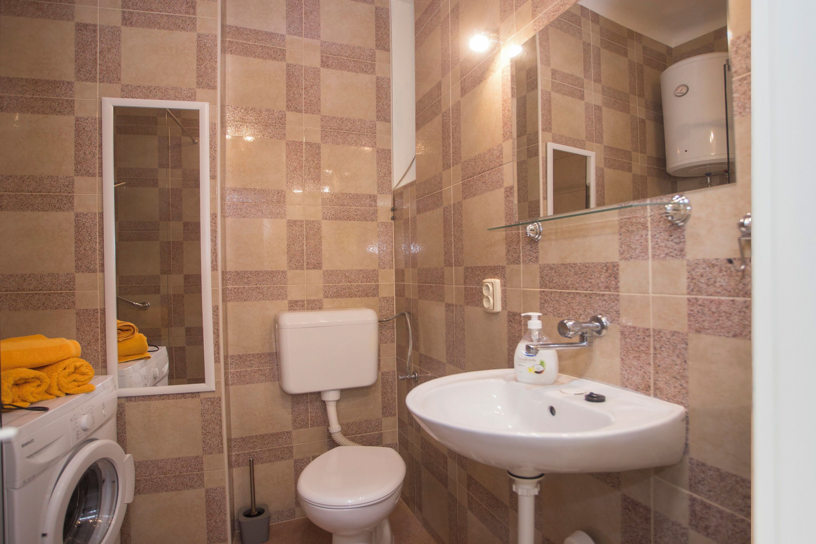 A bathroom with a washing machine, toilet, sink, and a glass shower enclosure.