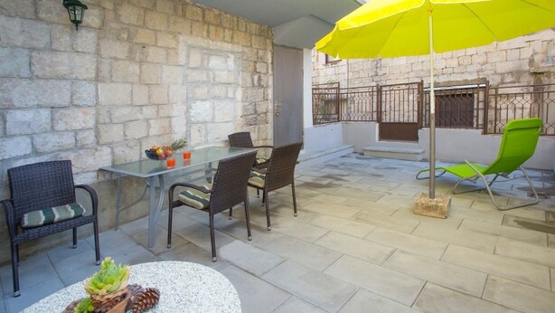 Una terrazza all'aperto con tavolo e sedie, un ombrellone giallo e un muro in pietra.