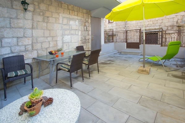An outdoor patio with a table and chairs, a yellow umbrella, and a stone wall. - Apartment Zdrav (Split)