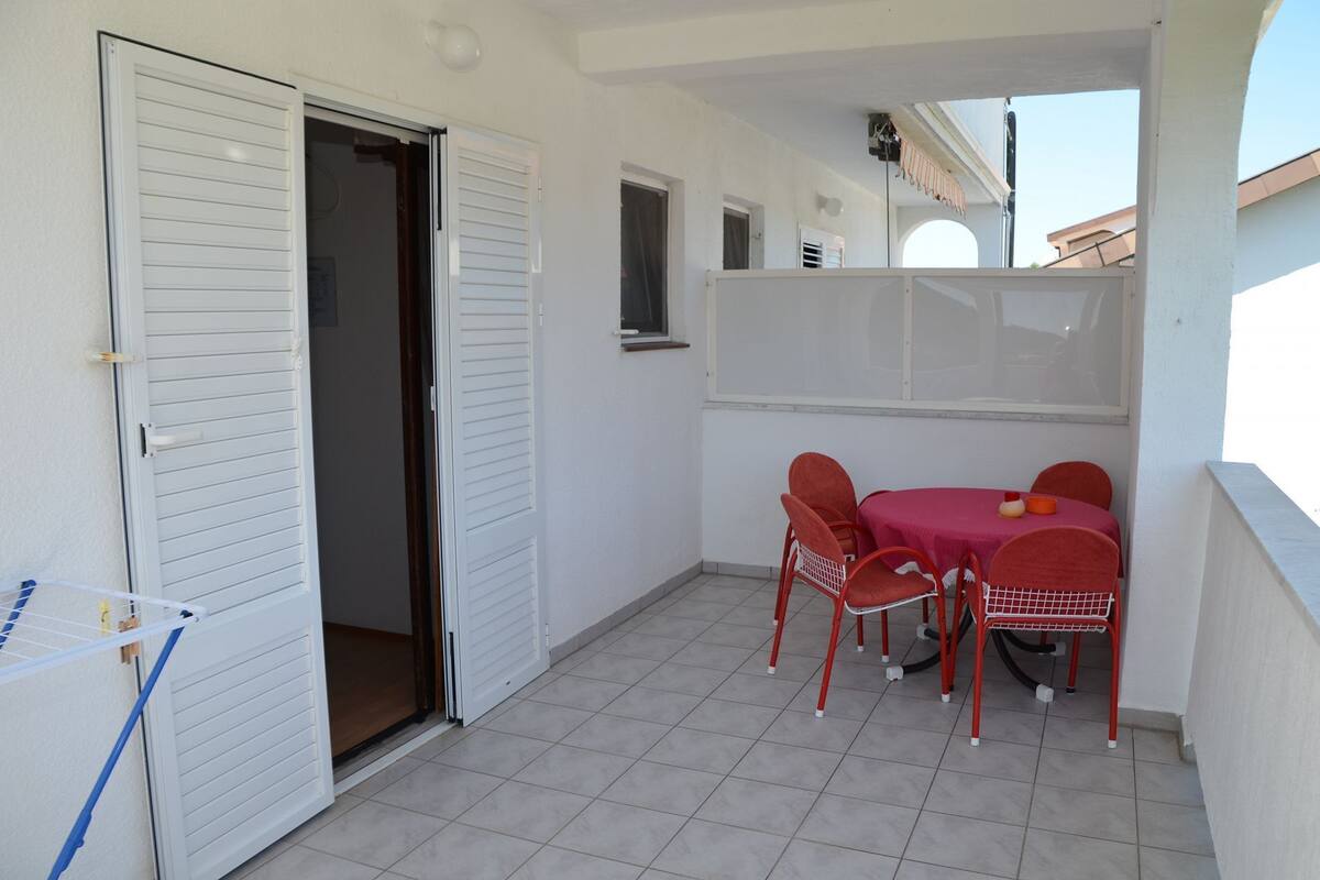 Un balcon avec une table et des chaises, une porte blanche et une petite fenêtre.