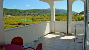 Un balcon donnant sur un paysage verdoyant et des montagnes. On y trouve deux chaises rouges et une table recouverte d'une nappe rose.