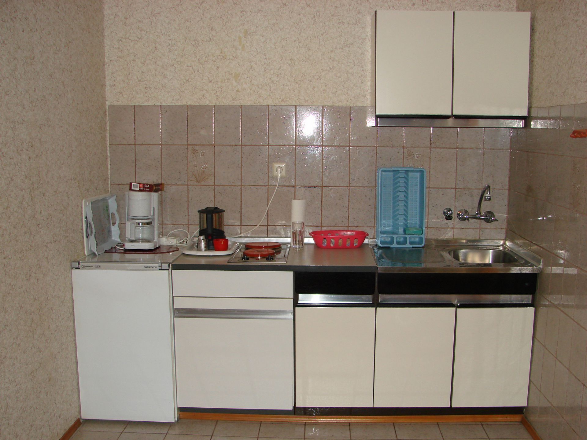 Eine kleine Küche mit Kühlschrank, Kaffeemaschine, Mixer und Spüle.