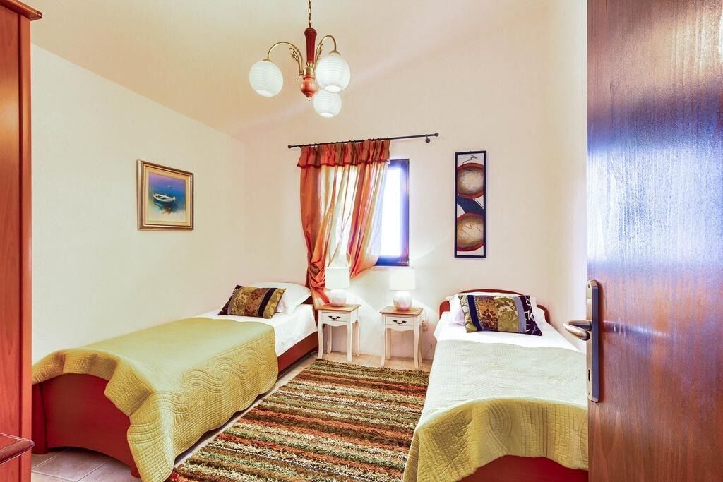 Habitación de hotel con dos camas individuales, una mesita, una silla, una ventana con cortinas y un cuadro en la pared.