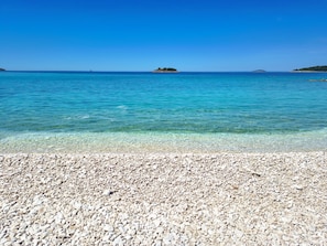 A pebbled beach with clear turquoise water and distant islands. - Apartments Lidija (Rogoznica)