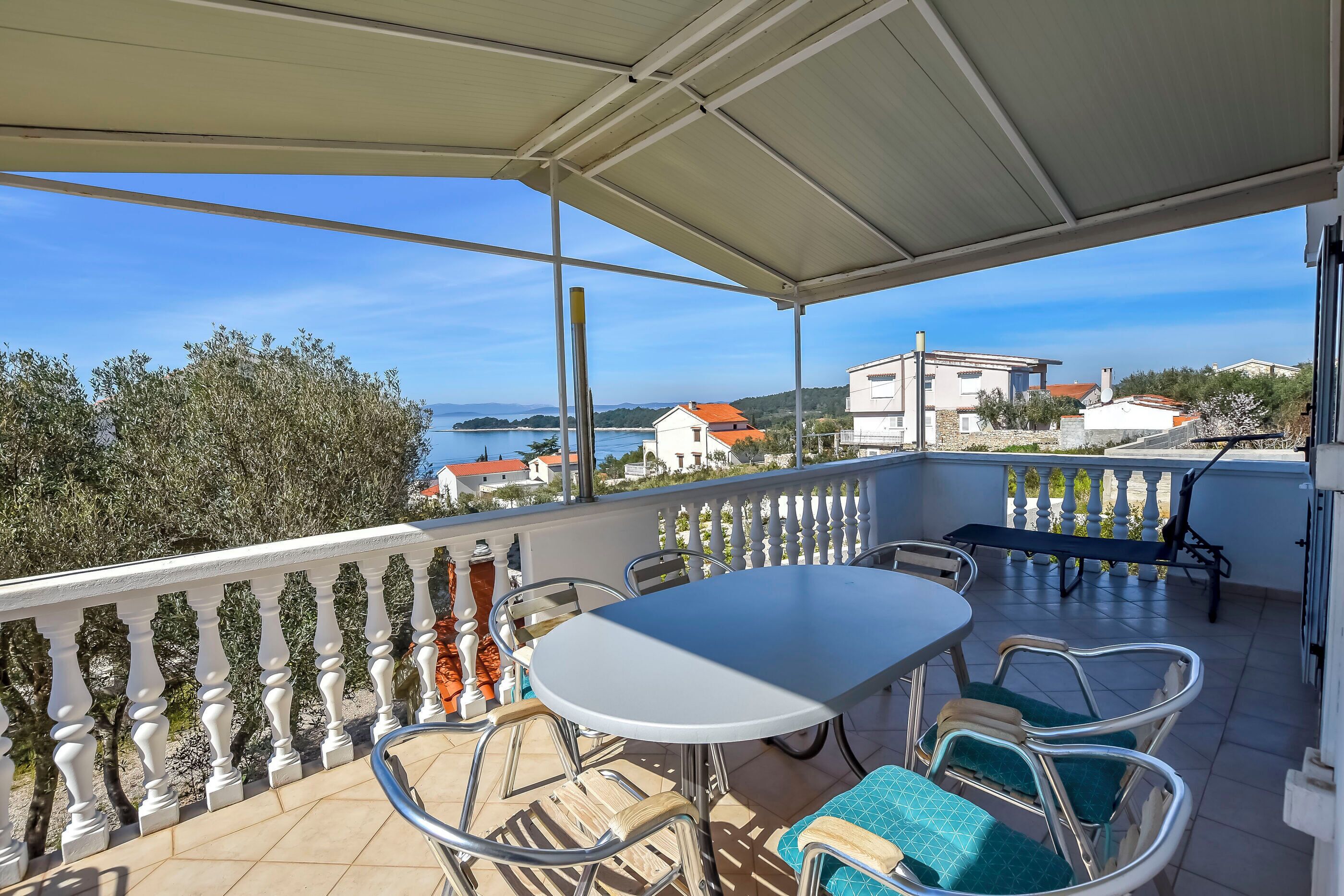 A balcony with a white table and chairs, a railing, and a view of the sea and buildings.
