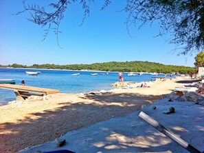 A beach with boats, a wooden pier, and people relaxing. - Apartment Glory (Pasman)