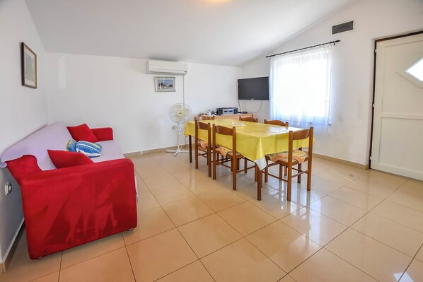 A room with a dining table, chairs, a red sofa, a TV, and a fan. - Apartment Glory (Pasman)