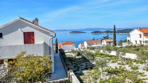 Ein Küstendorf mit weißen Häusern und roten Dächern, einem klaren blauen Himmel und Blick auf das Meer und ferne Inseln.
