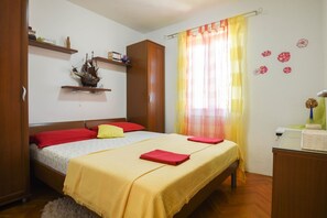 Un dormitorio con cama, armario de madera y dos estantes con libros y un modelo de barco.