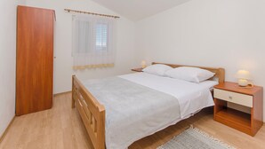 Ein Schlafzimmer mit einem hölzernen Bett, weißer Bettwäsche, einem Nachttisch mit Lampe, einem Holzschrank und einem Fenster mit Jalousien.