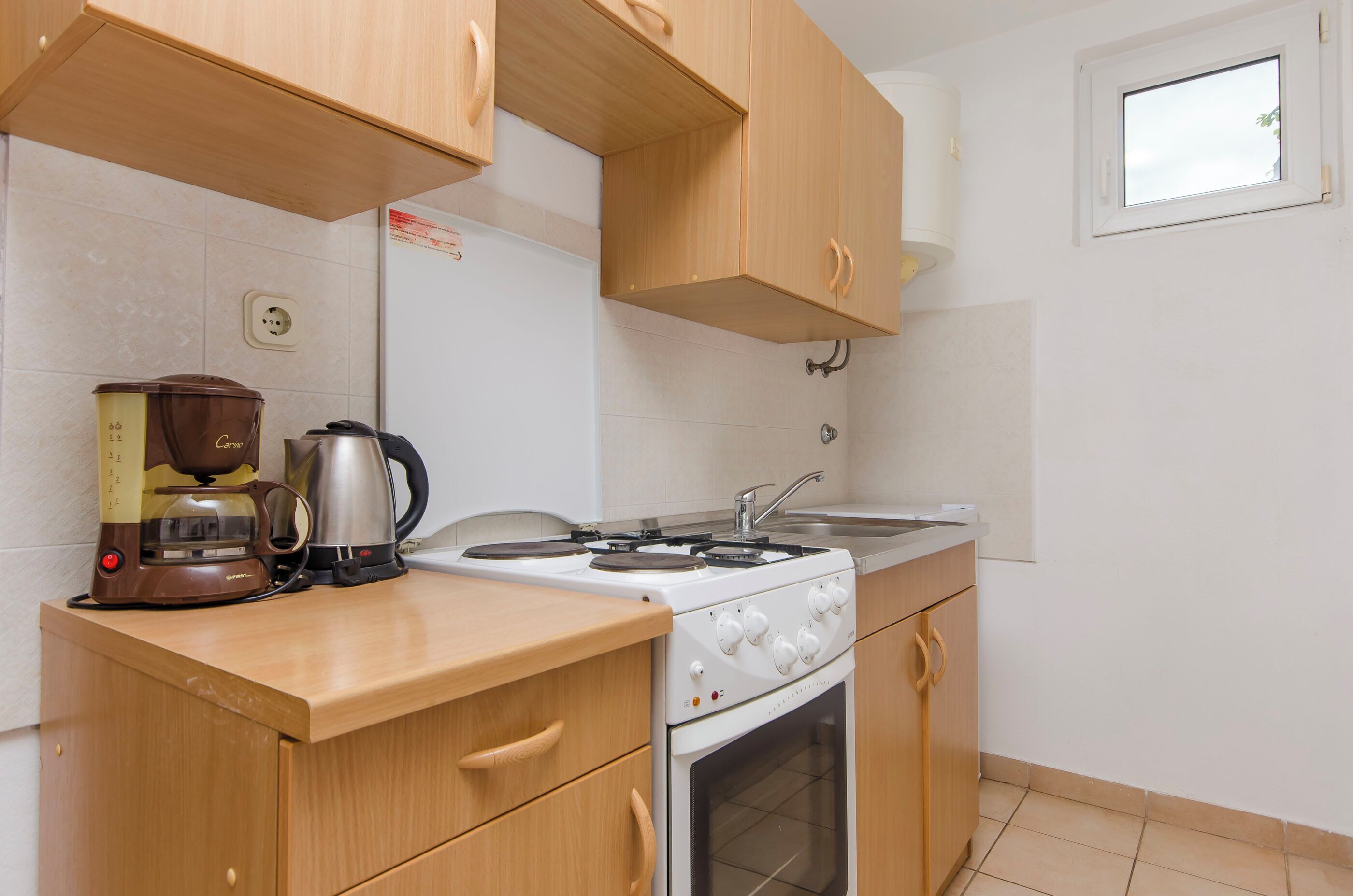 Una piccola cucina con mobili in legno, un fornello, una macchina da caffè e un frigorifero.