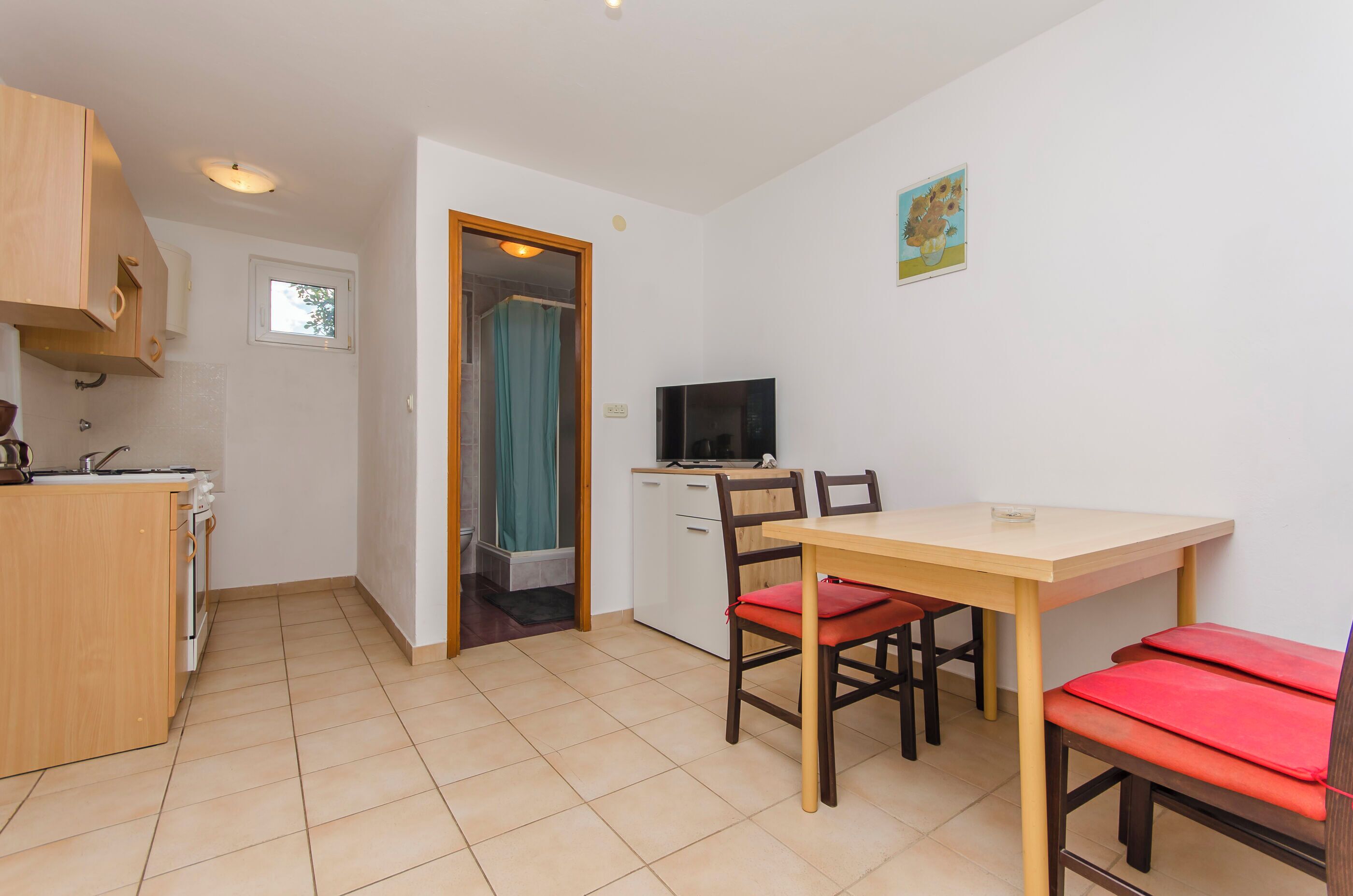 A compact kitchen with a dining area, a TV, and a small window.