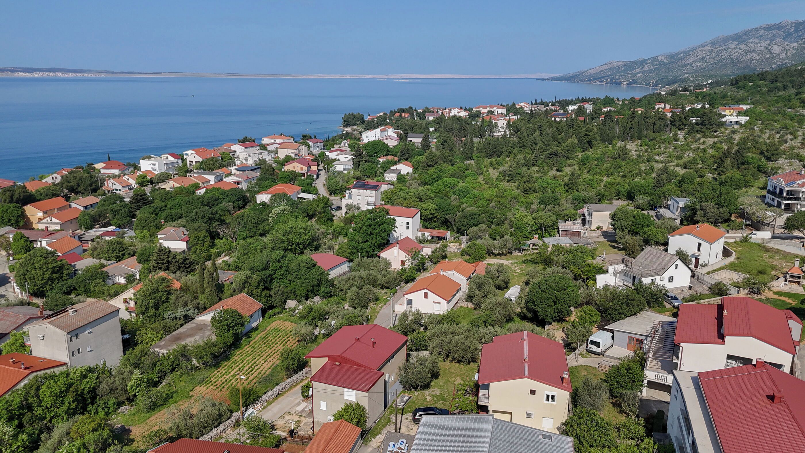 A coastal residential area with houses, some with red roofs, and a view of the sea.