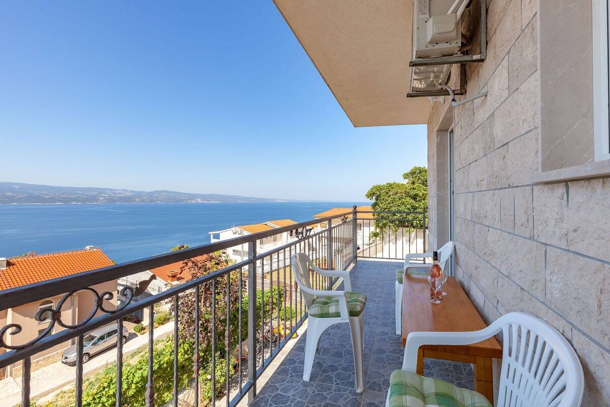 A balcony with a view of the sea, a table with chairs, and a window with an air conditioning unit.