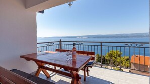 Ein Holztisch mit zwei Weingläsern und einer Flasche auf einem Balkon mit Blick auf ein Gewässer.