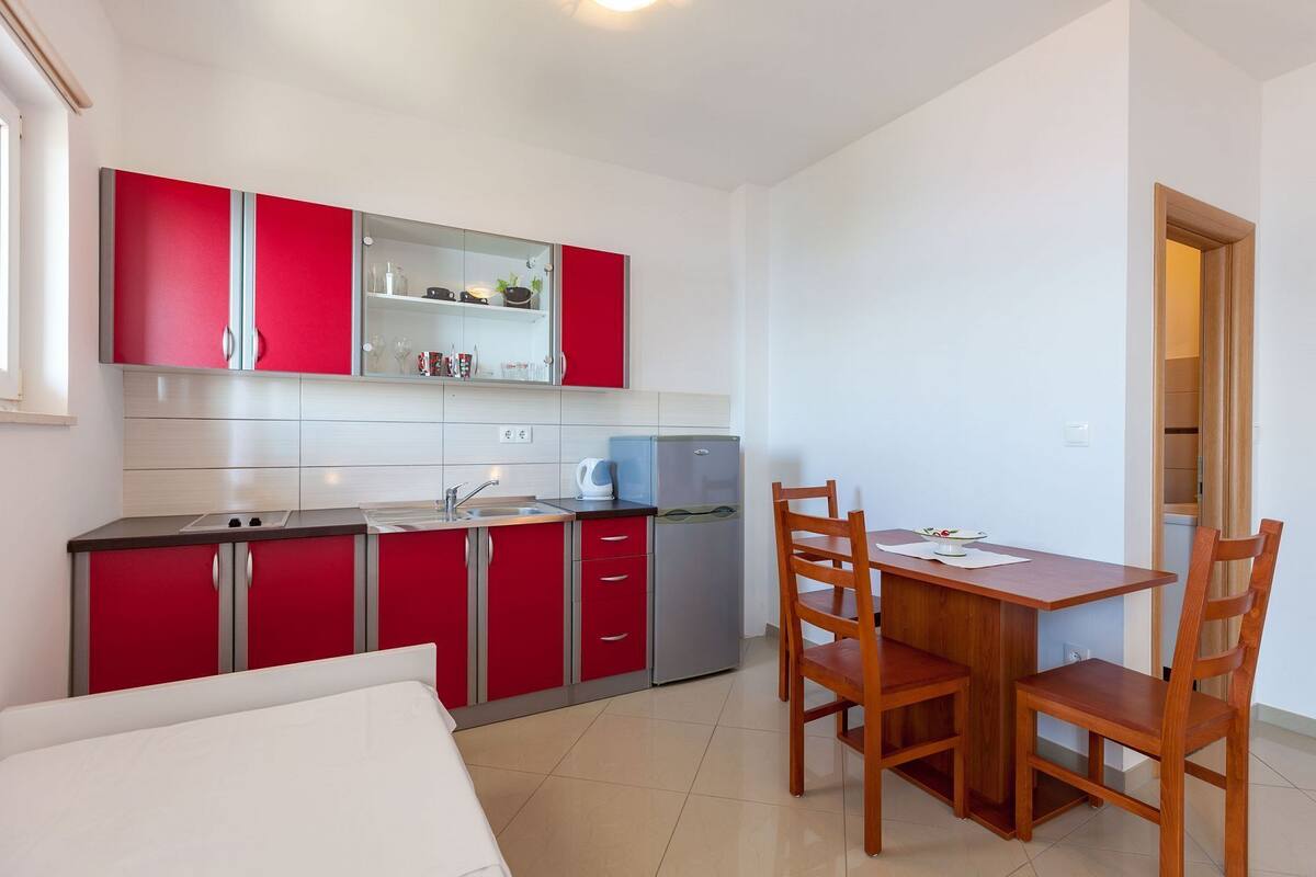 A compact kitchen with red cabinets, a sink, a refrigerator, and a dining area with a table and chairs.