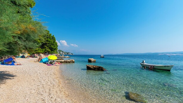 Ein Strand mit klarem Wasser, Felsen und einem Boot.