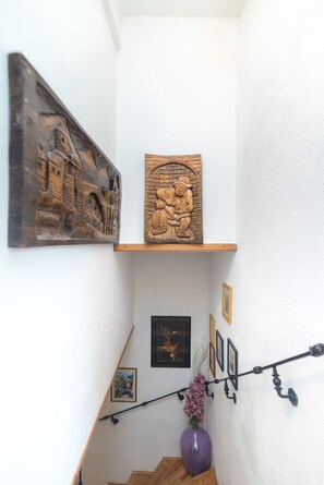 Eine Treppe mit Holzgeländer, eine violette Vase mit rosa Blumen und zwei Holzschnitzereien an der Wand.