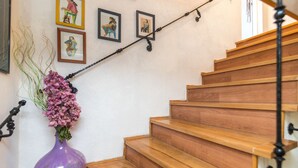 Un escalier en bois, et sur le palier, un vase violet rempli de fleurs.