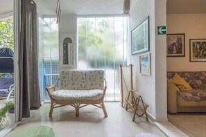 A room with a wicker chair, a sofa, a green rug, and a window with curtains. - House Zeljko (Sucuraj)