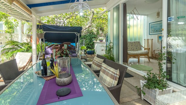 Un espace extérieur abrité, aménagé avec une table, des chaises et des plantes en pot.