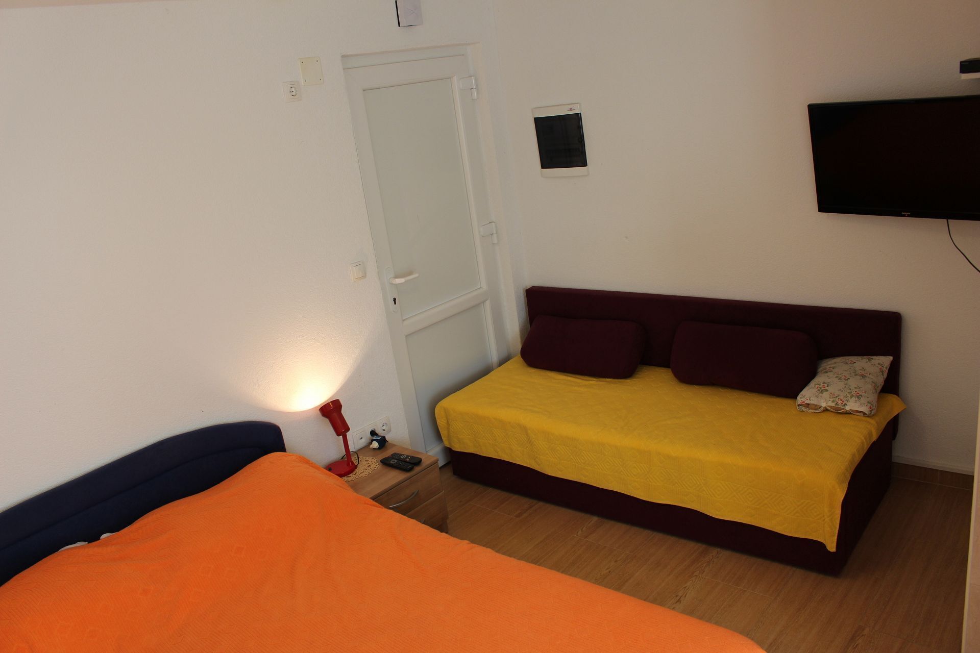 A bedroom with a bed, a bedside table, a lamp, a television, and a door.