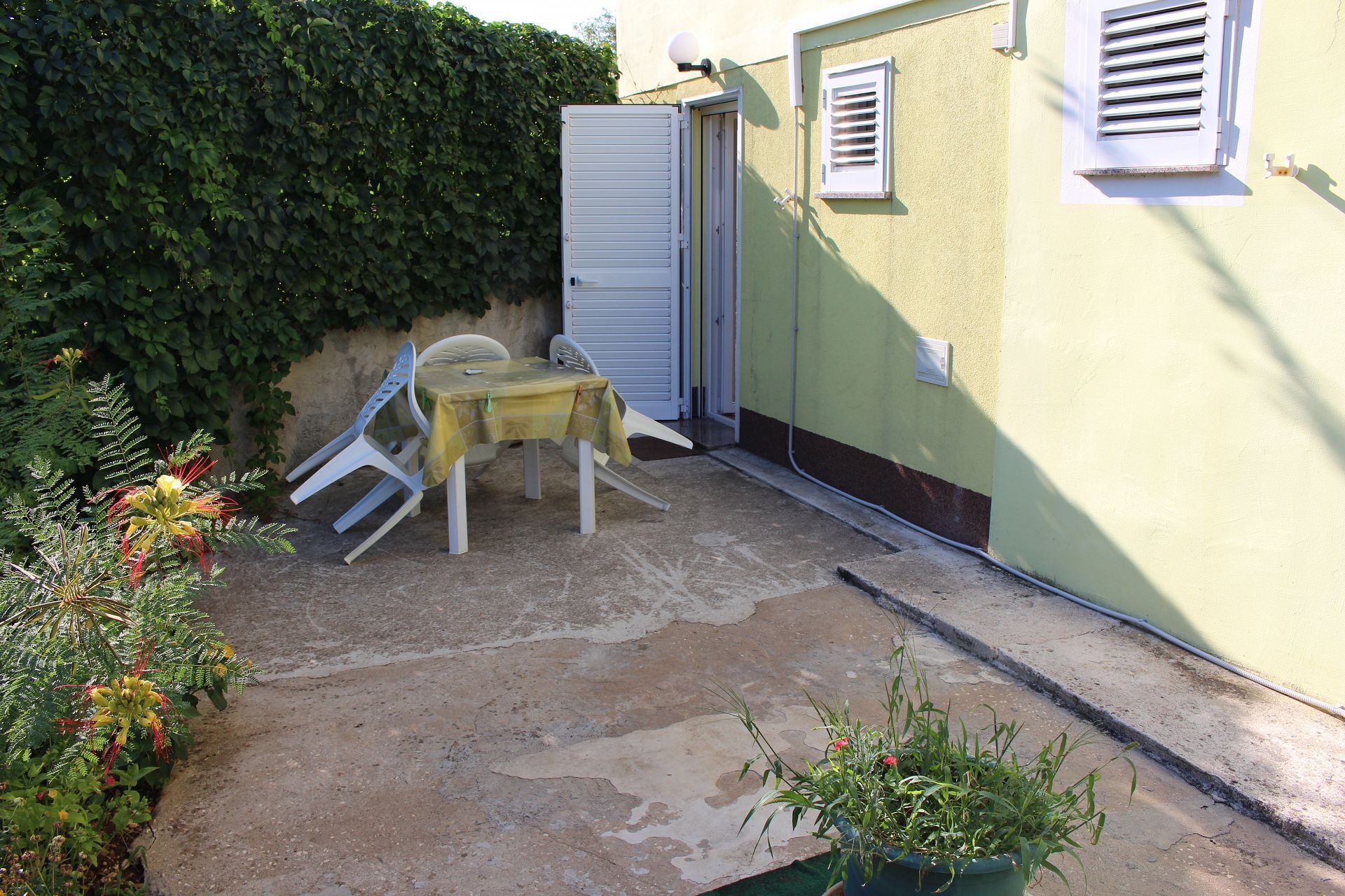 A small outdoor patio with a table and chairs, a door, and a wall with shutters.
