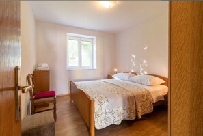 A bedroom with a wooden bed, a window, a chair, and a bedside table. - Apartments Mir (Nin)