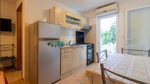Une cuisine compacte équipée d’un réfrigérateur, d’une cuisinière et d’un four à micro-ondes. On y trouve une table à manger avec des chaises, ainsi qu’un téléviseur fixé au mur.