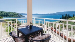 A balcony with a table and chairs, overlooking a coastal landscape with mountains and a body of water. - Apartments Ljuba (Slivno)