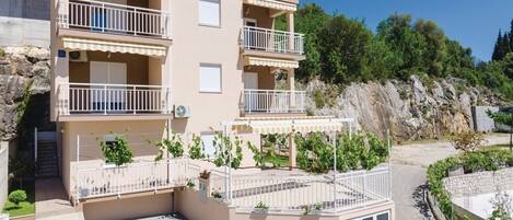 A multi-story building with balconies, a paved courtyard, and a rocky hillside background.