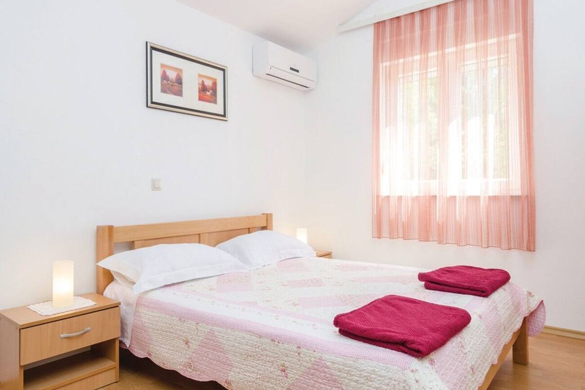 A bedroom with a bed, nightstands, a picture on the wall, and an air conditioning unit.